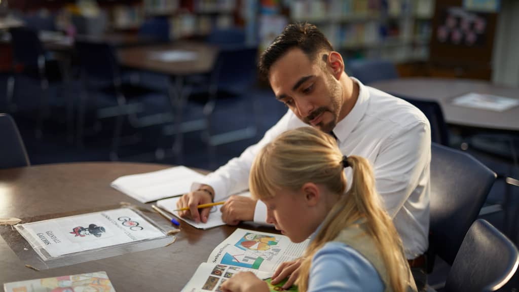 Male teacher sitting at desk with student working through problem together