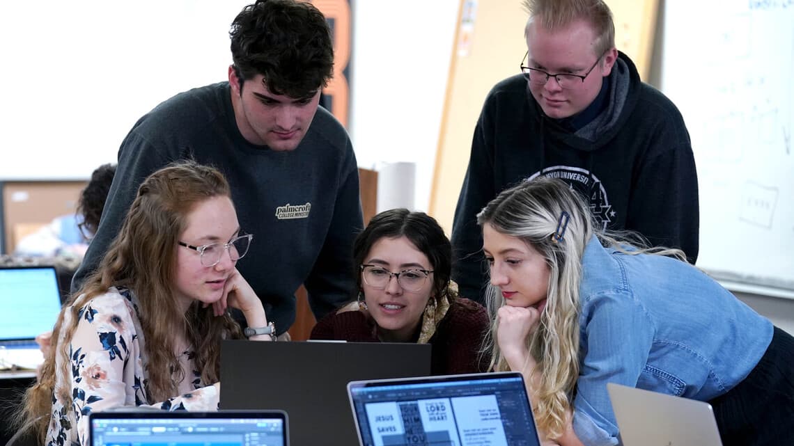 Group of students gather around a computer screen when working on digital and advertising design