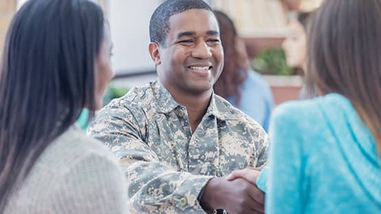 Military man in fatigues shakes hand of brunette female