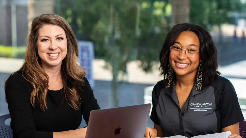 Two honors college students sitting and smiling next to eachother