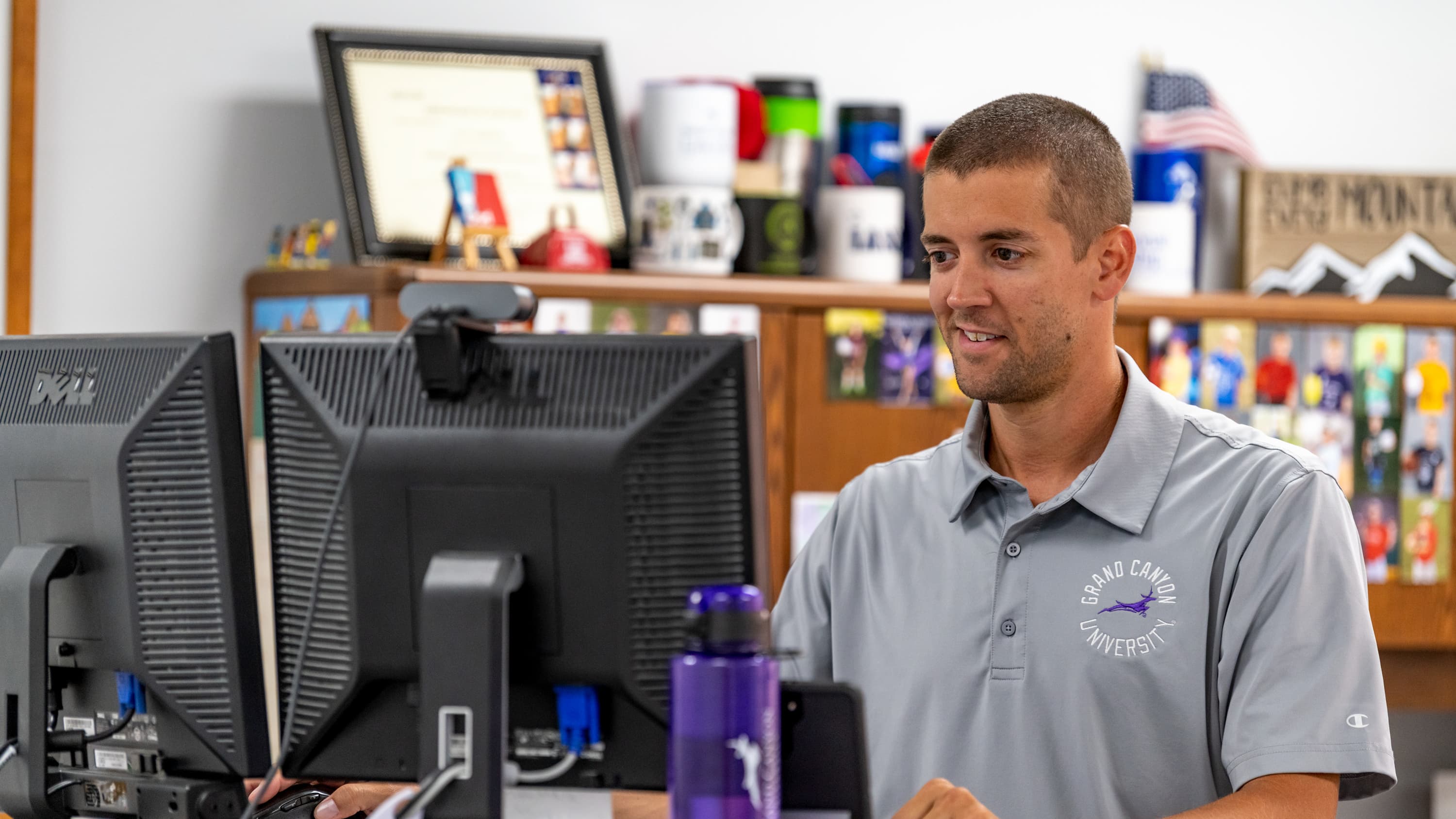 Male master's teaching degree graduate sits in classroom at desk smiling