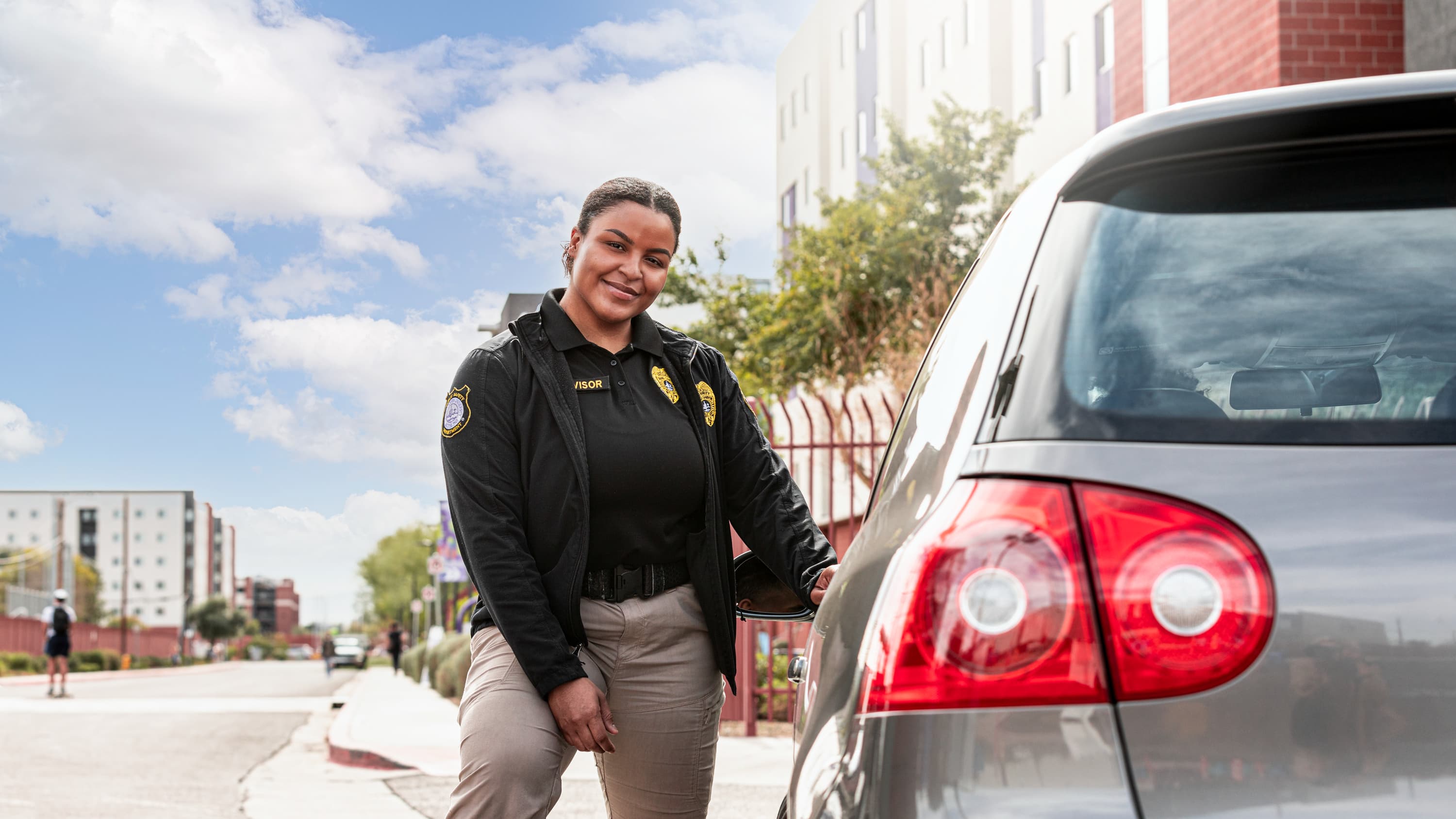 Female legal studies degree graduate smiling next to car as Public Safety Officer