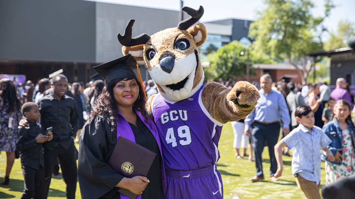 Graduate smiling in photo with GCU mascot Thunder