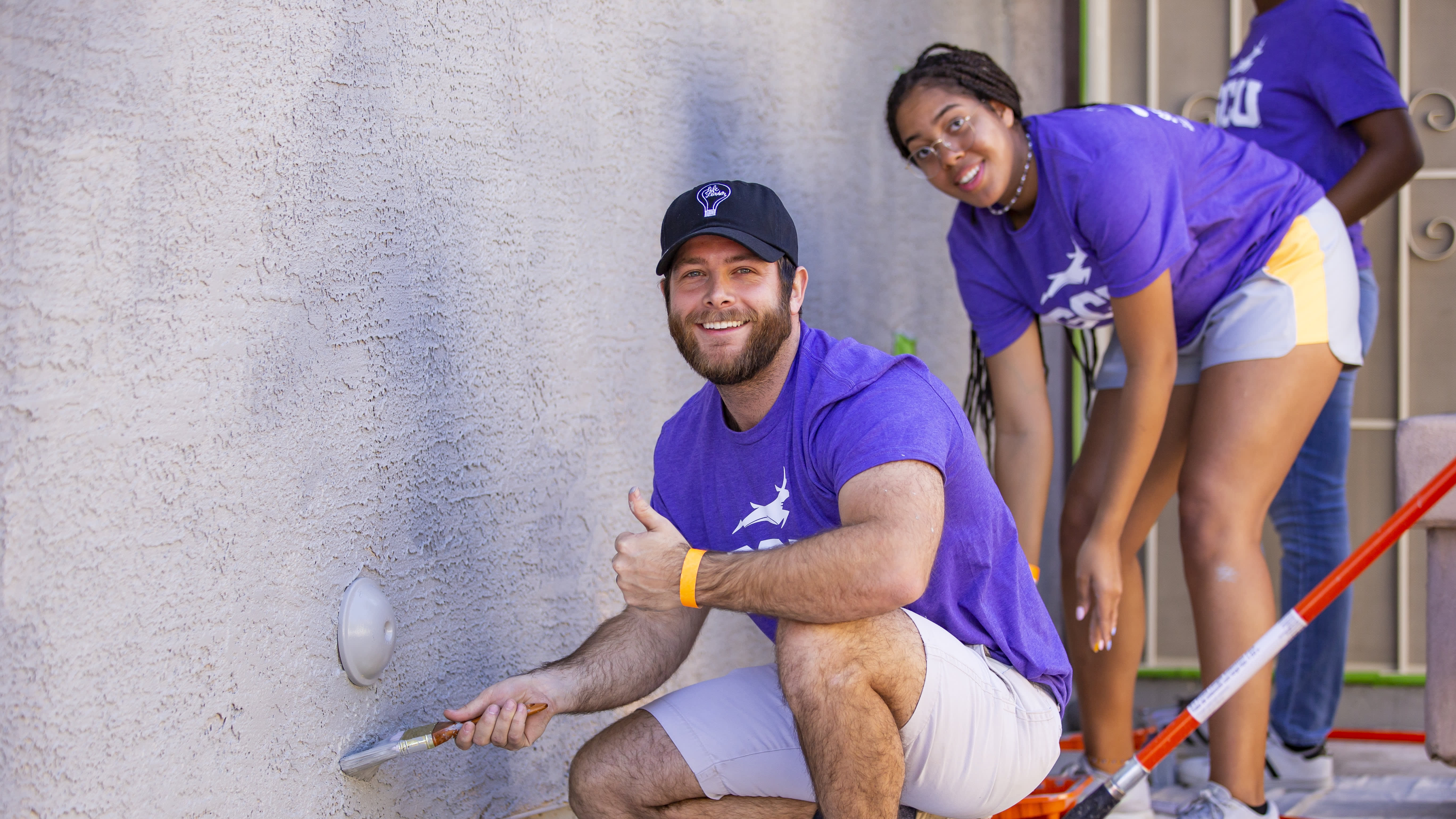 Two students in purple shirts painting wall