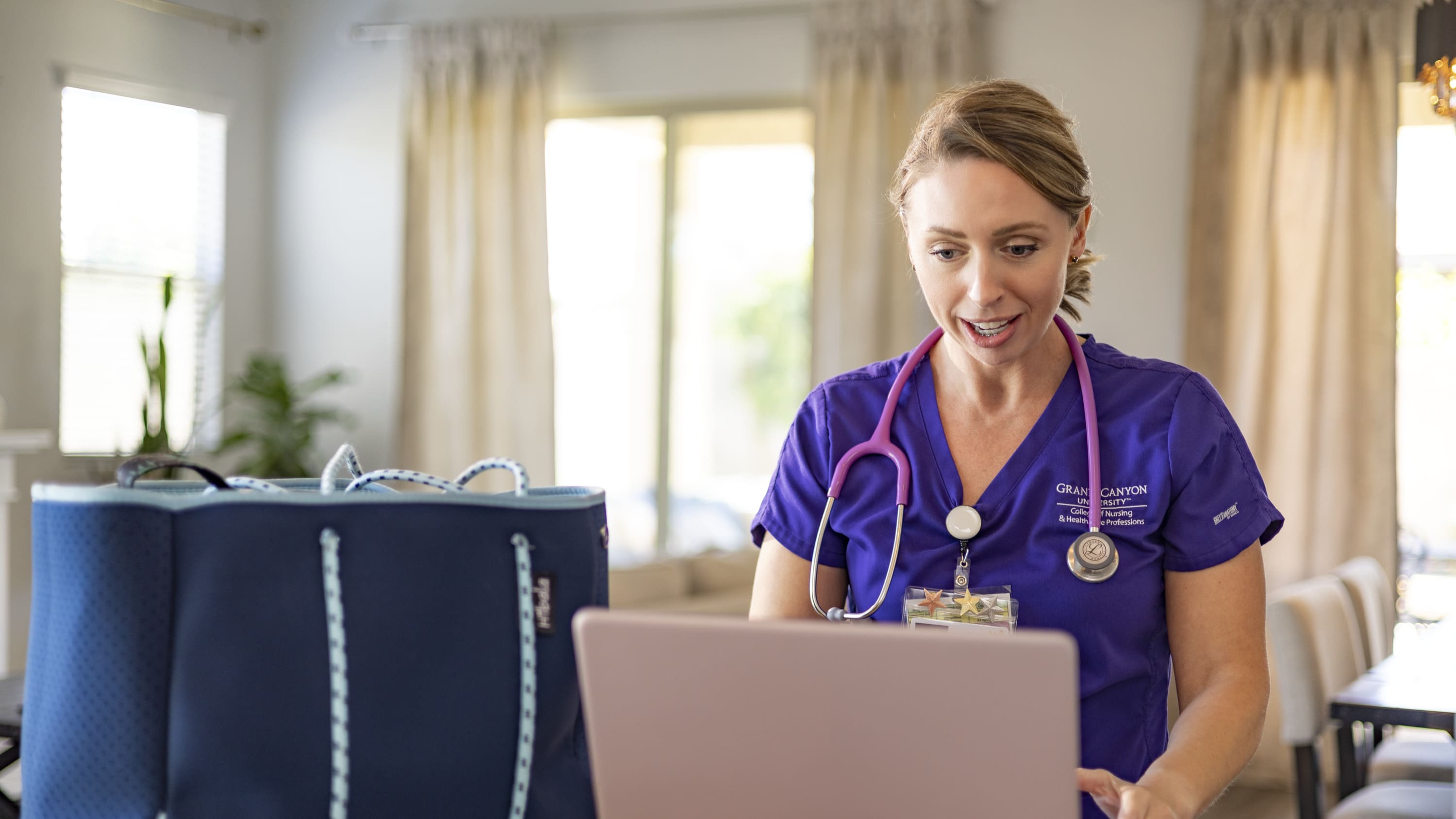 Female student in GCU scrubs completing online healthcare certificate at home