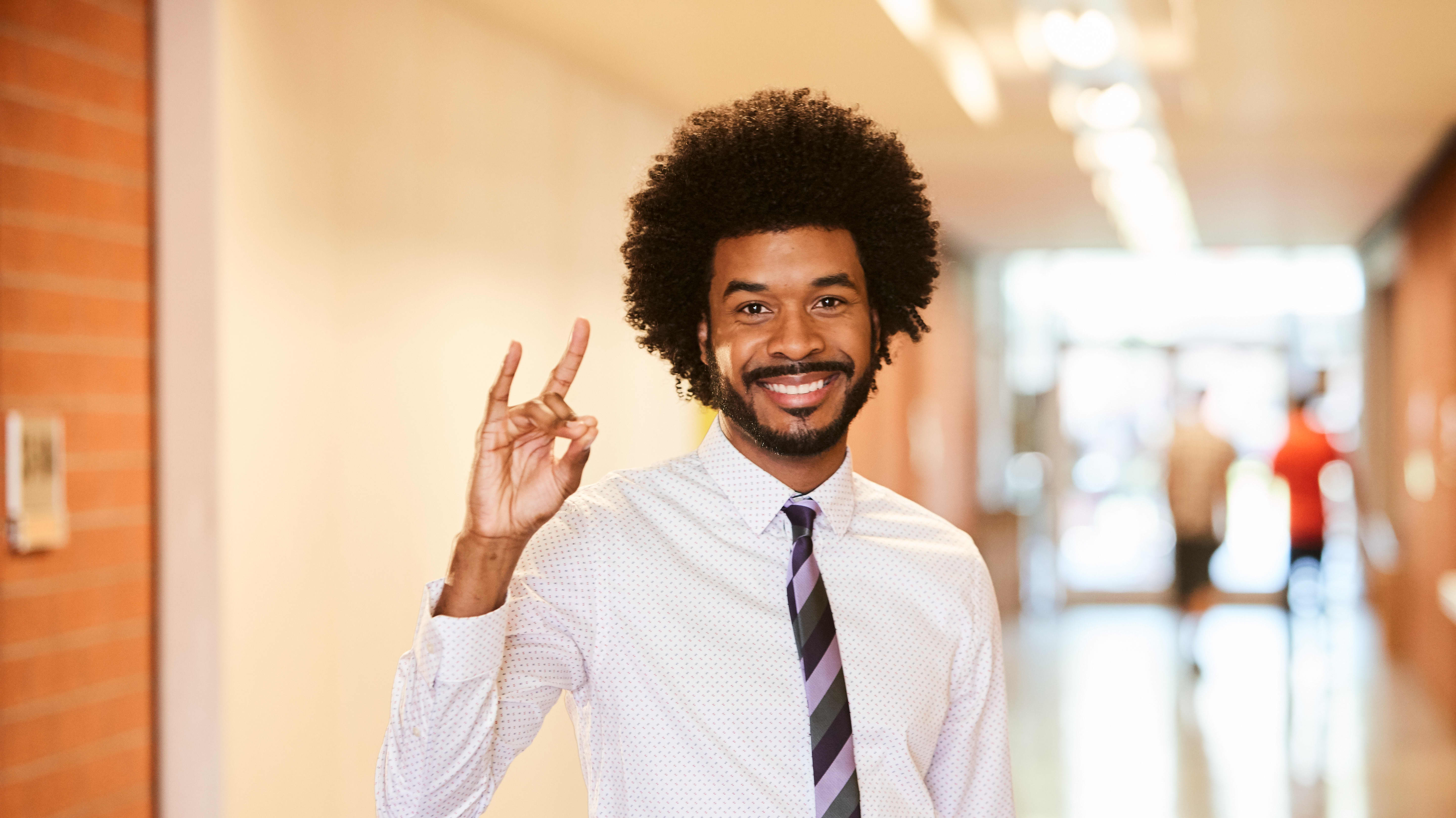 Male bachelor's in education major smiling in school hallway holding Lopes Up hand sign