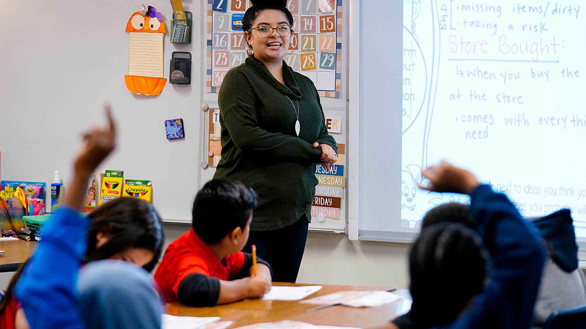 Early secondary teacher goes over language arts with the kids with hands raised to answer questions