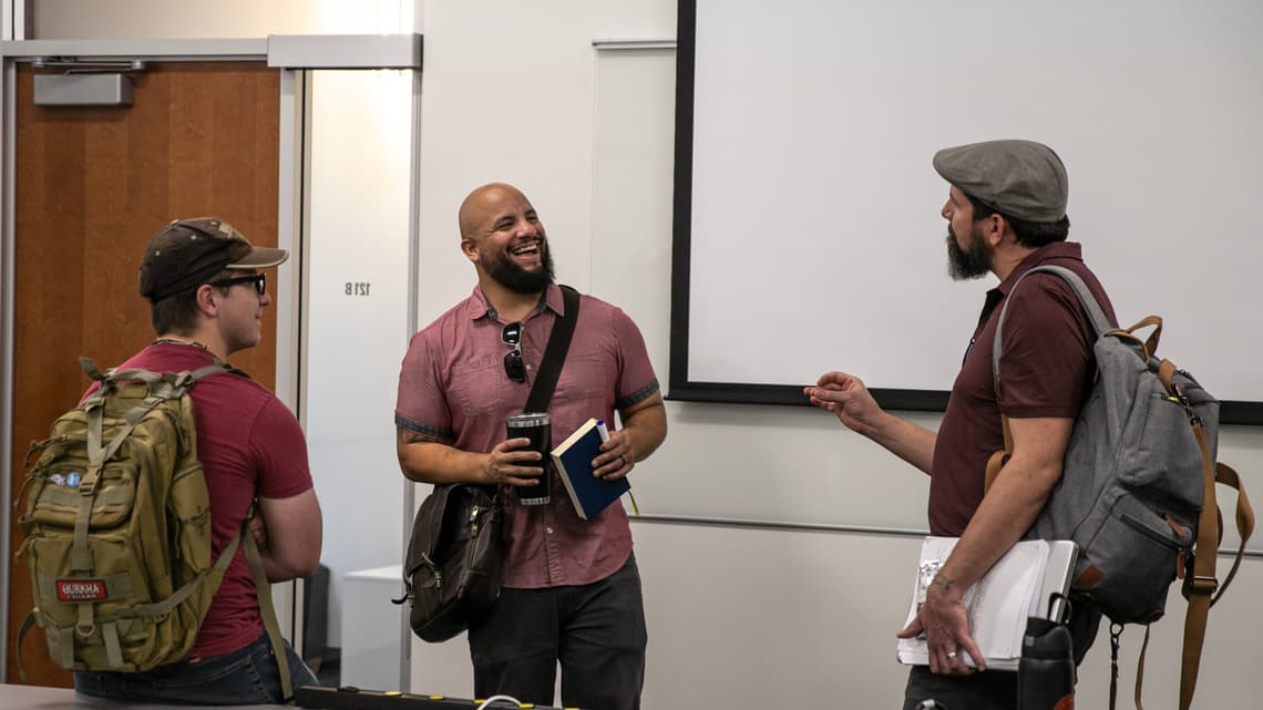 Three male seminary students talking after class near the white board