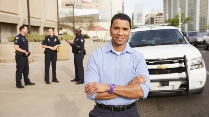 Male criminal justice degree graduate standing in police uniform in front of car