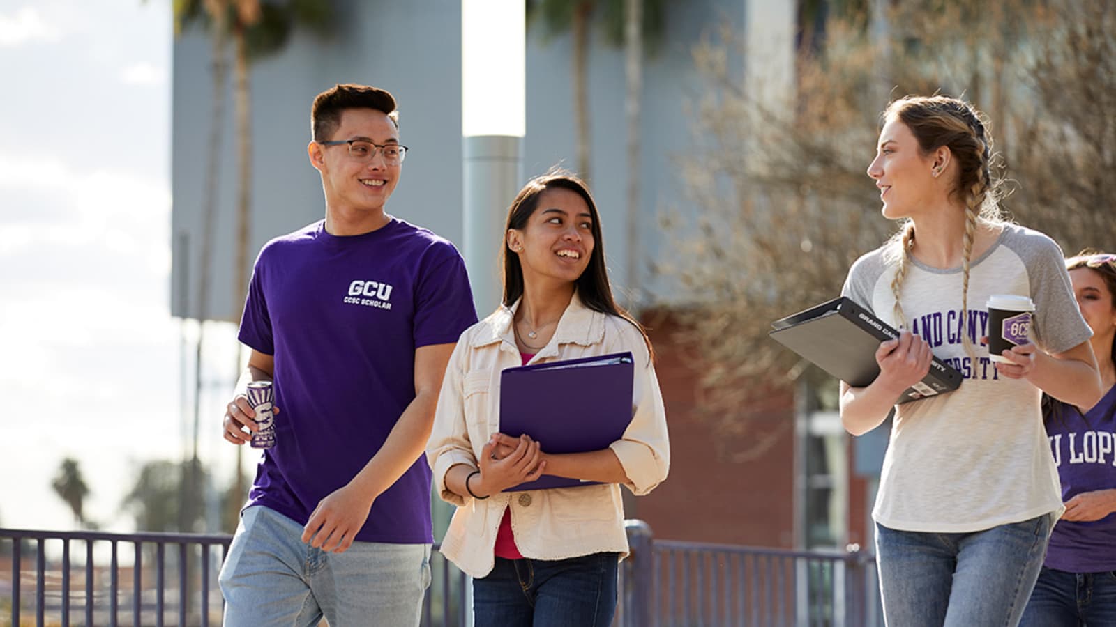 Tall asian male in a dark purple GCU tshirt walks along side two females of mixed ethnicities to listen to them talking