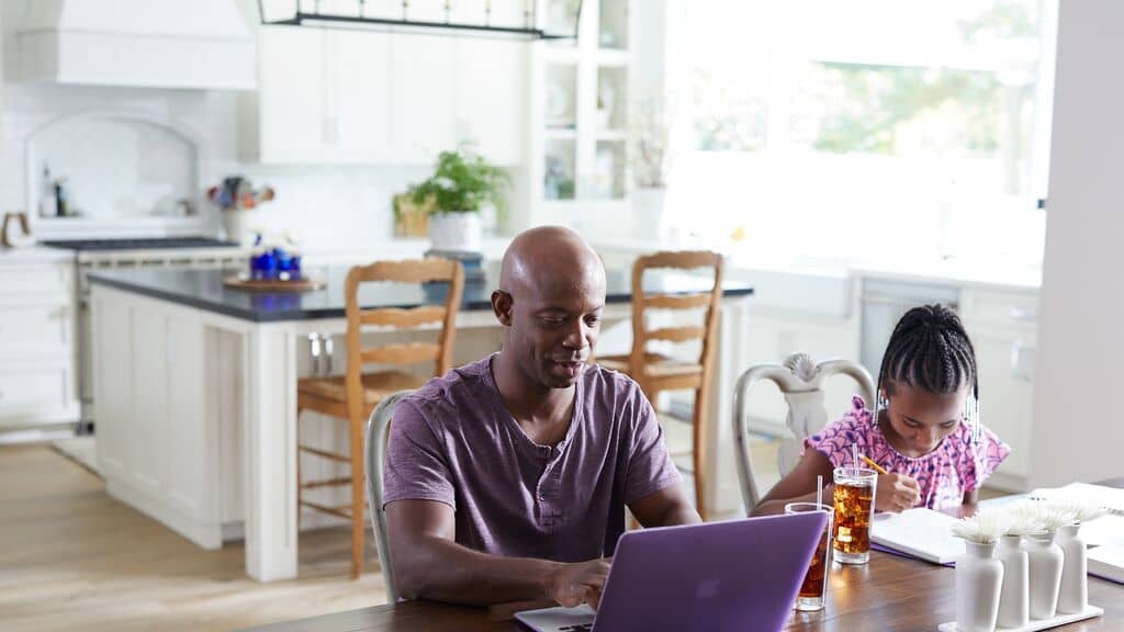 man using a laptop in the kitchen next to his daughter