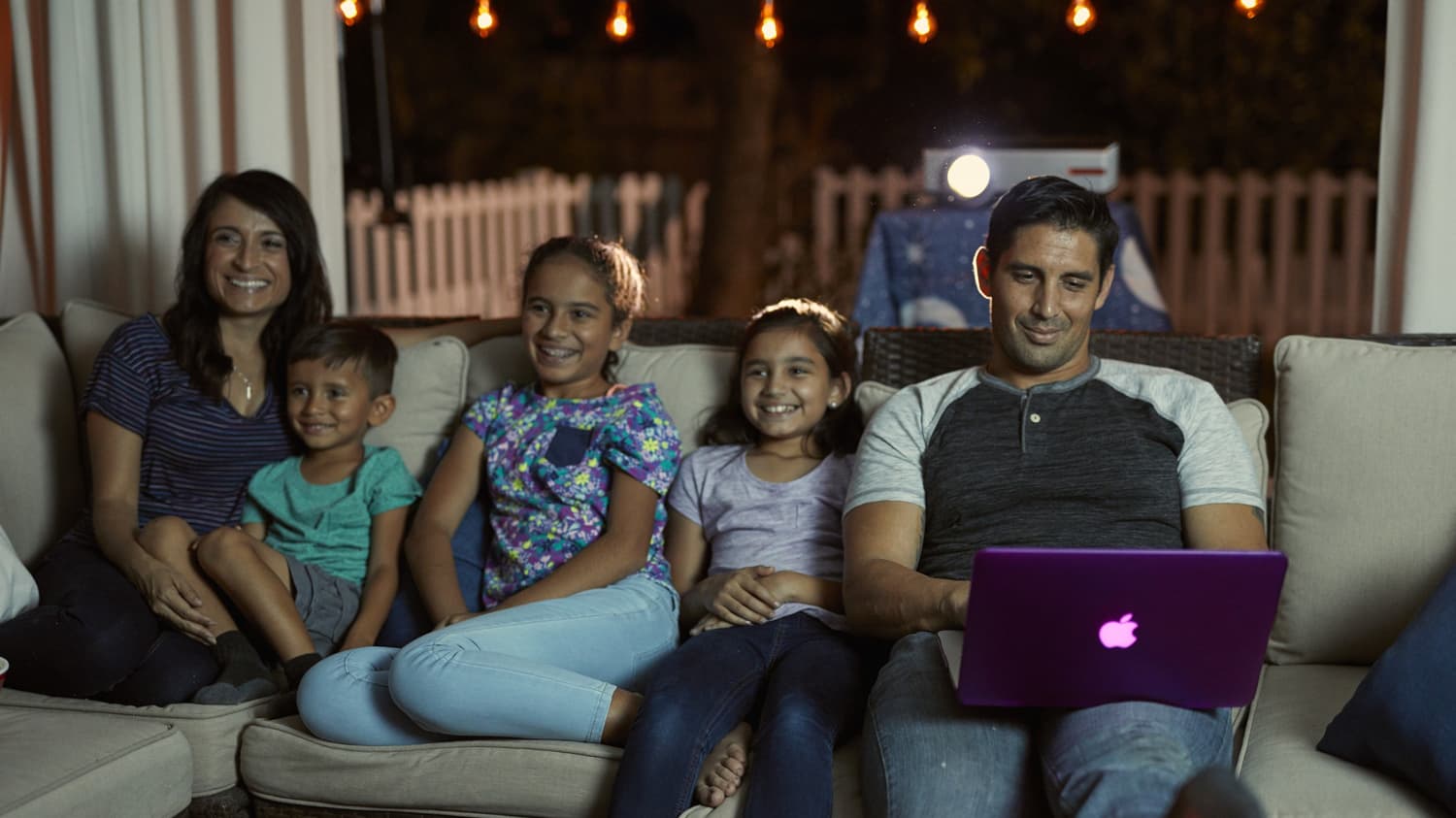 a husband works on homework while watching a movie with his family