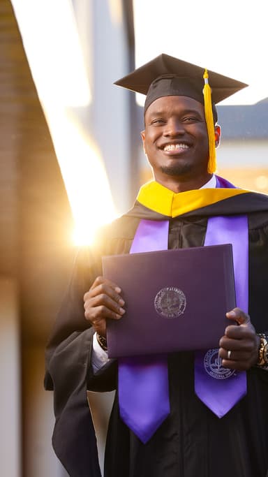 Male online degree graduate smiling at sunset on GCU's campus in cap and gown