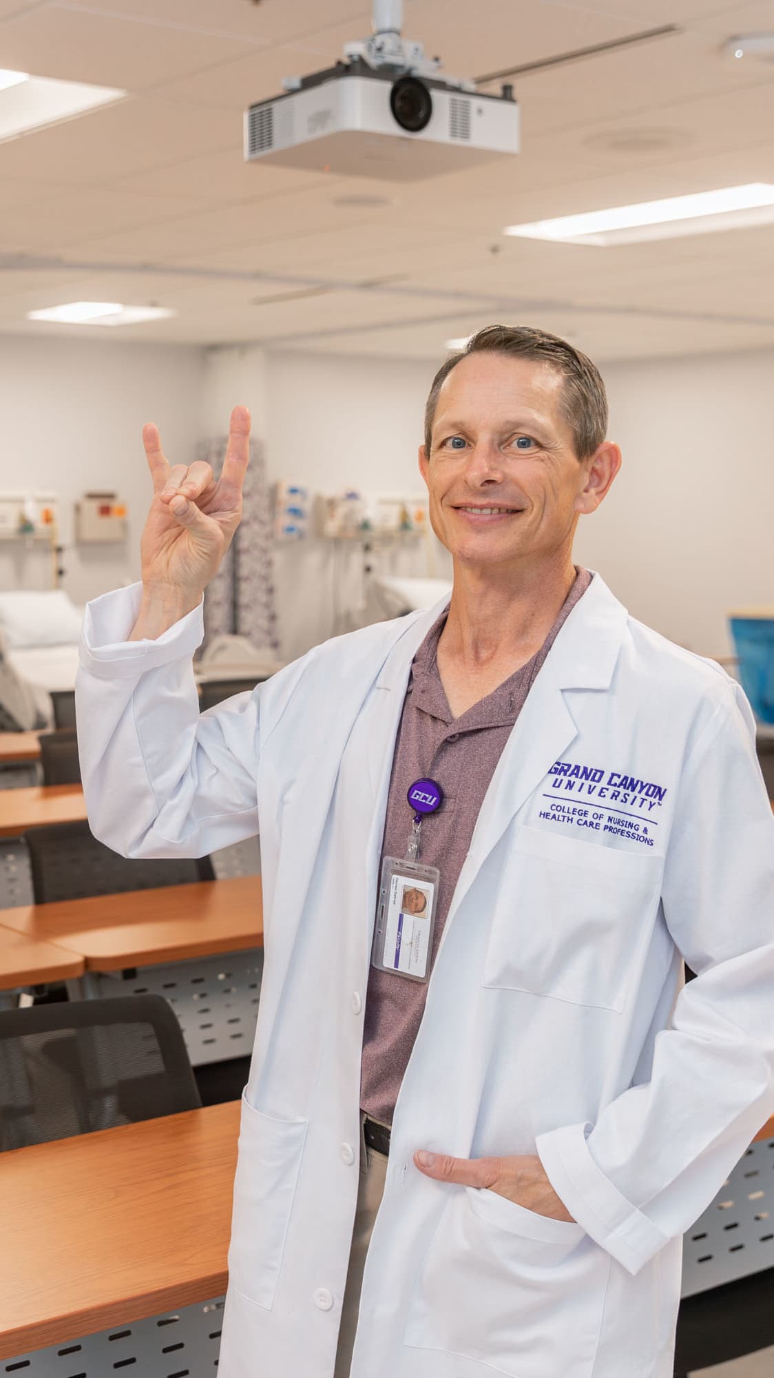 Male BSN degree graduate smiling in classroom wearing GCU white coat