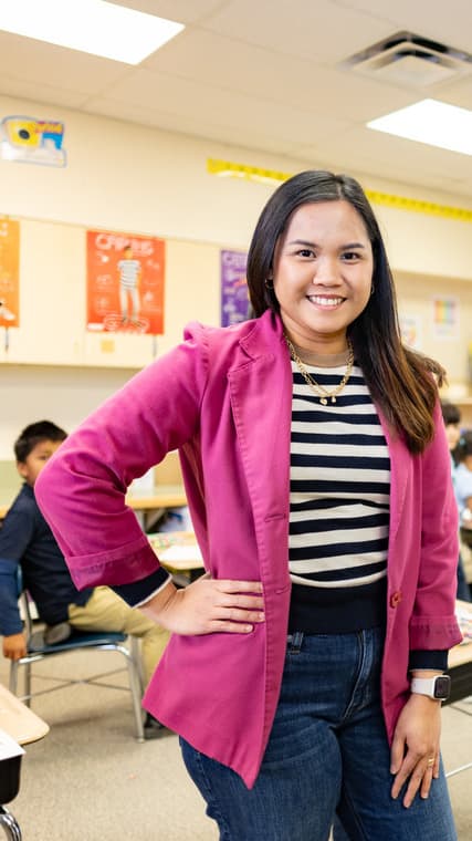 Teacher in pink jacket standing and smiling in front of a classroom