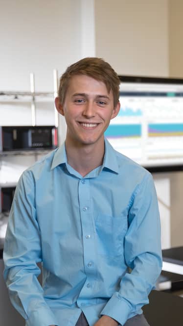 Computer Science Student Sits at Computer and Gives Lopes Up Hand Gesture