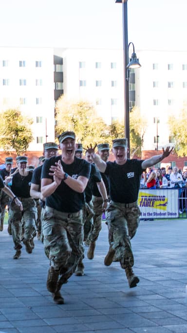 Group of ROTC cadets in black t-shirts and fatigue caps and pants run into open doors