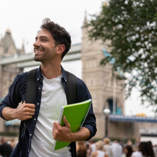 Young man in a foreign city holding a notebook and backpack