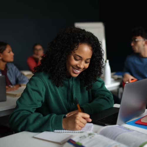 young female student smiling while writing in notebook