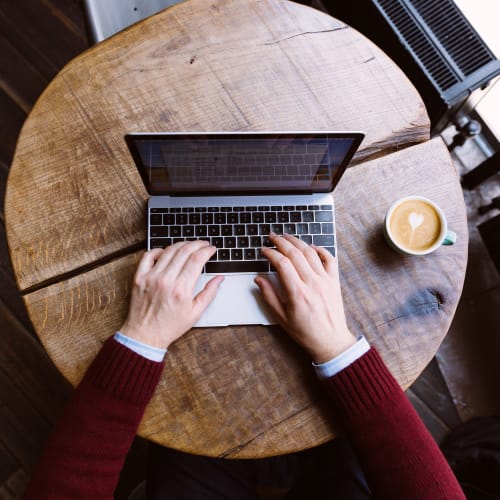 Typing on laptop with coffee next to it in a cafe