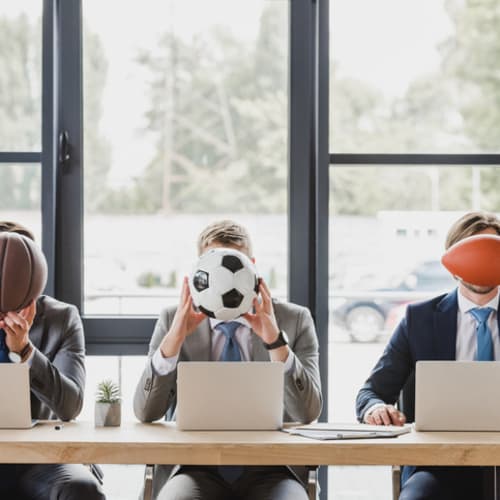 Three office workers holding different sports balls in their hands