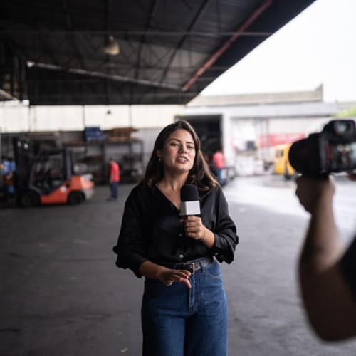 Young female broadcast journalist reporting on location