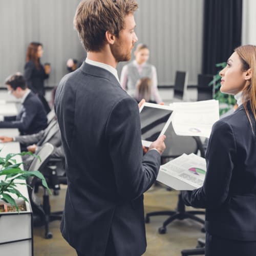 Business woman and man talking in a busy office setting 