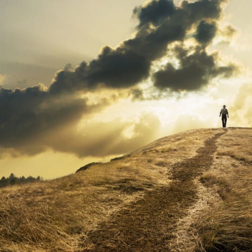 Person walking on a hill with the cloudy sky in the background