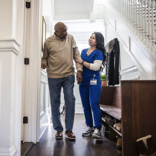 Female nurse aiding a senior man with walking at home