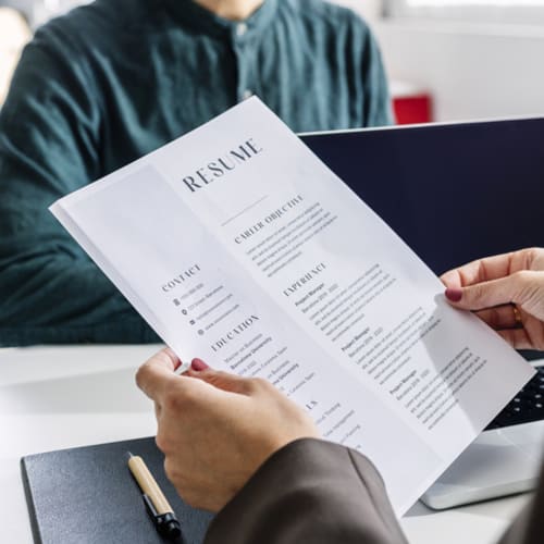 Hands of recruiter holding resume in front of candidate at desk - stock photo