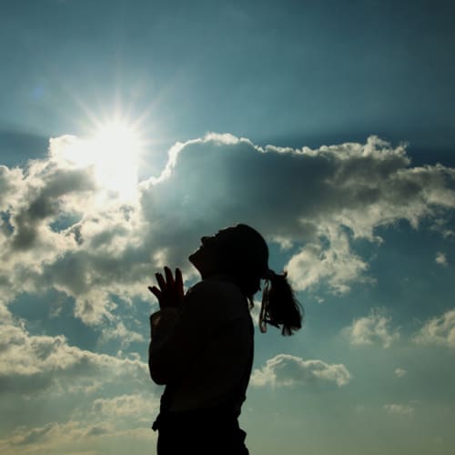 Female praying and looking up to the sky and sun