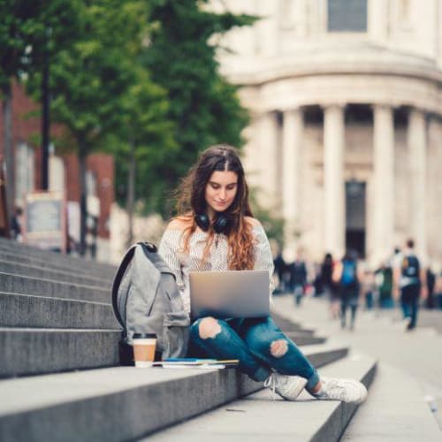 student sitting on stairs and typing on a laptop