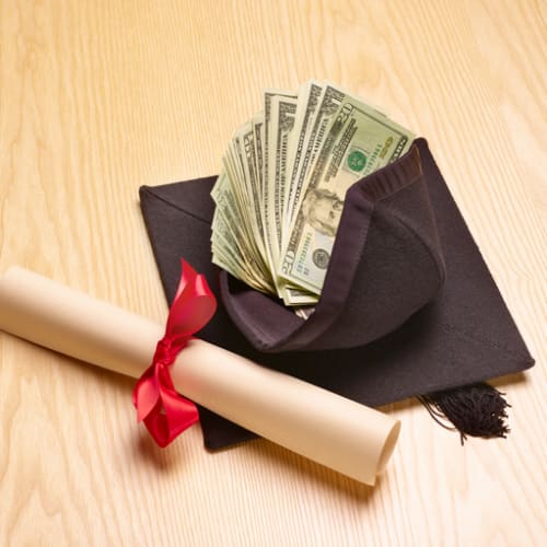Rolled diploma and graduation cap with dollars inside