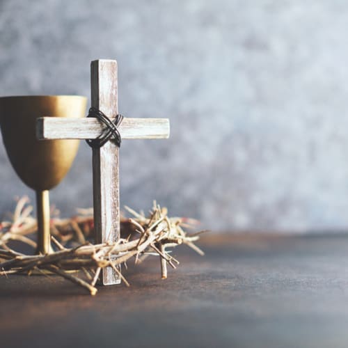 A cross sits with a wine glass and crown