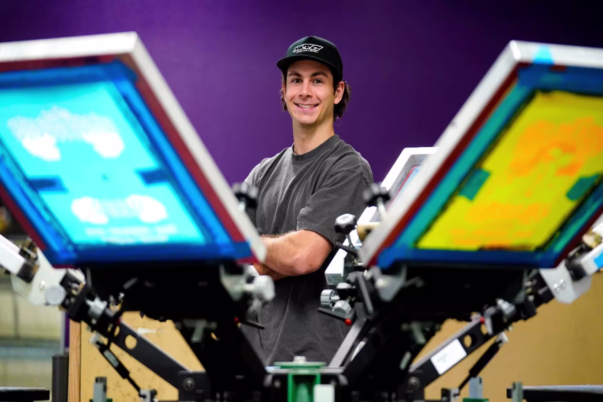 Entrepreneurship student in hat standing behind products with his arms crossed