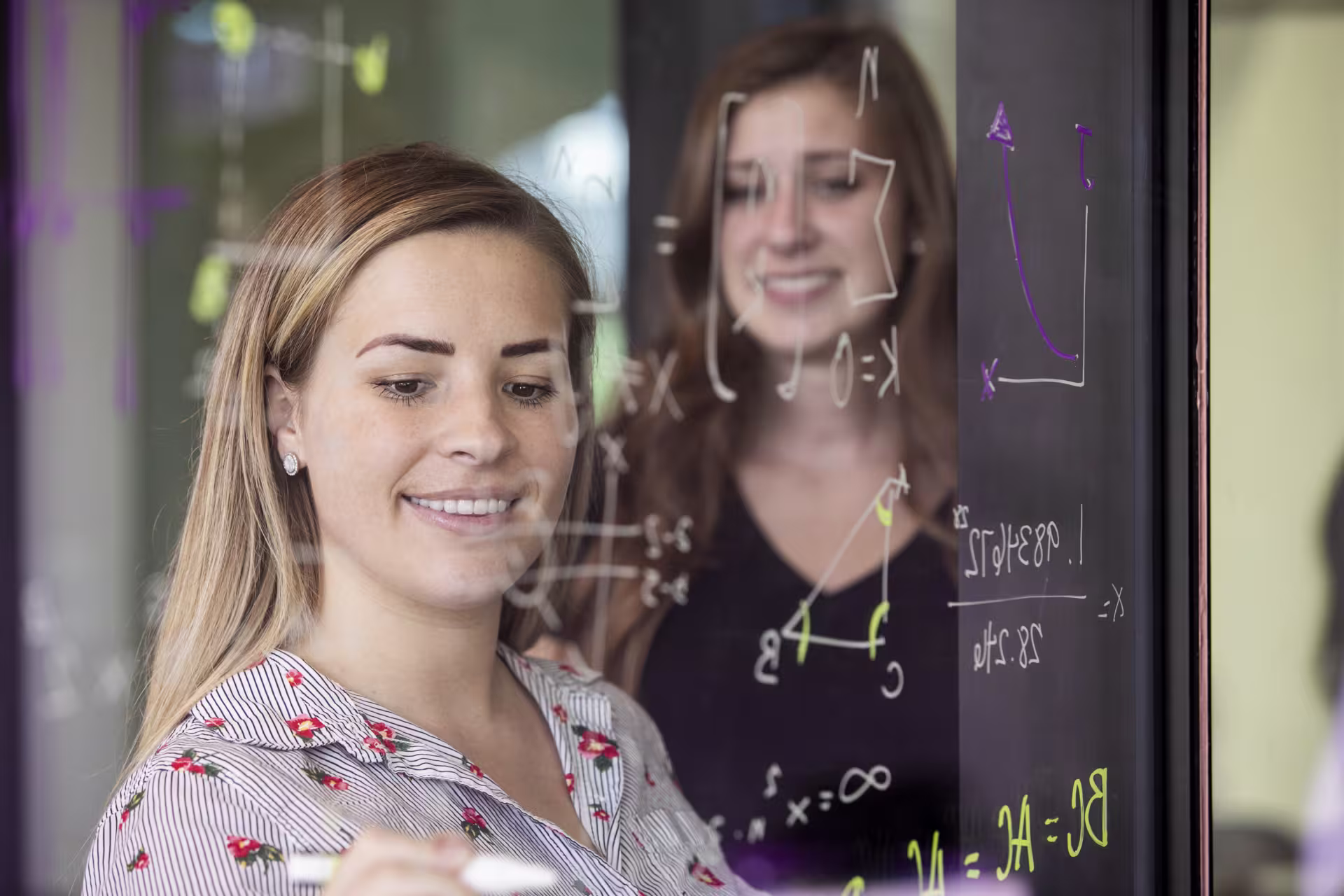 Two GCU math students writing on glass wall