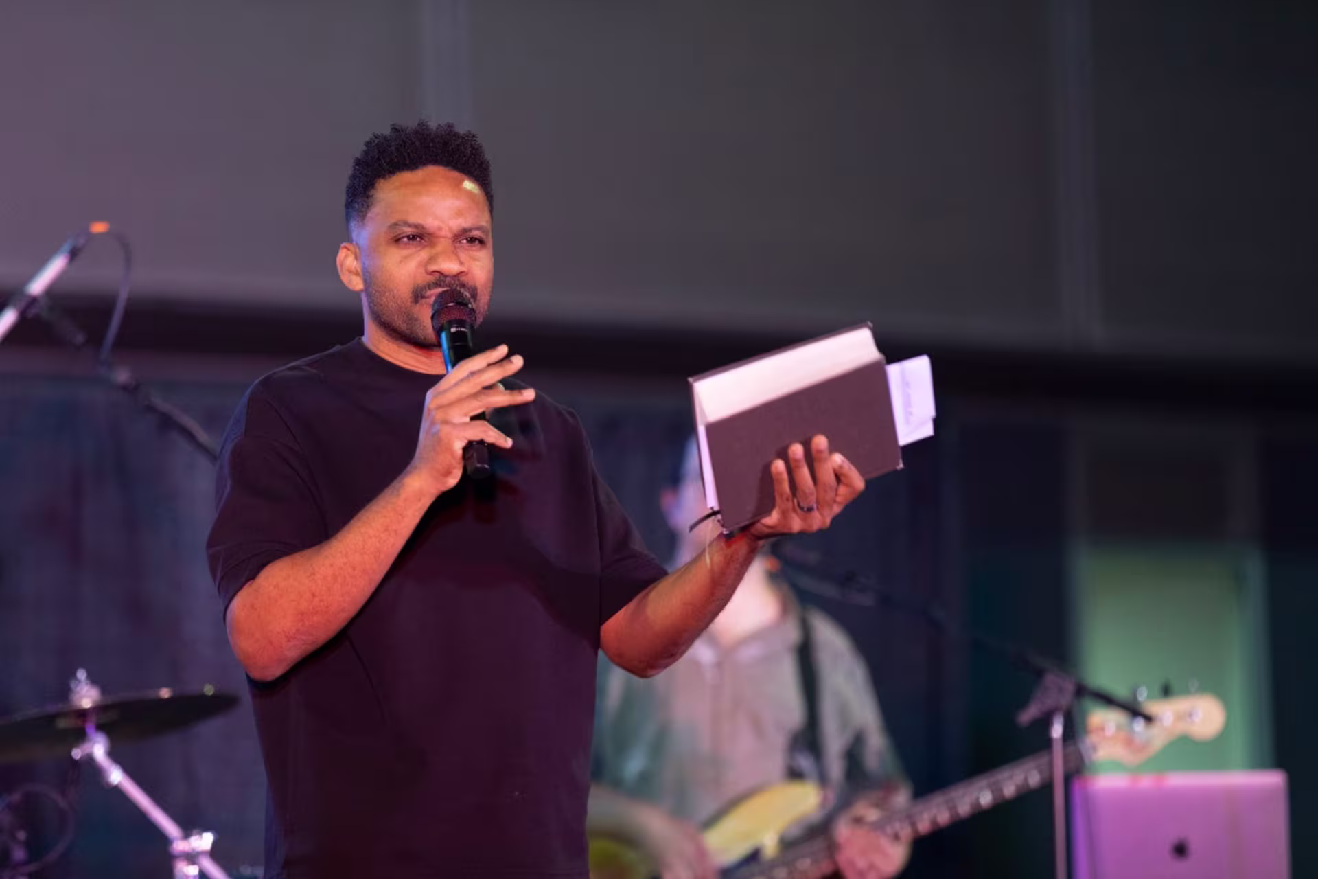 Pastor on stage holding microphone and bible with hands up