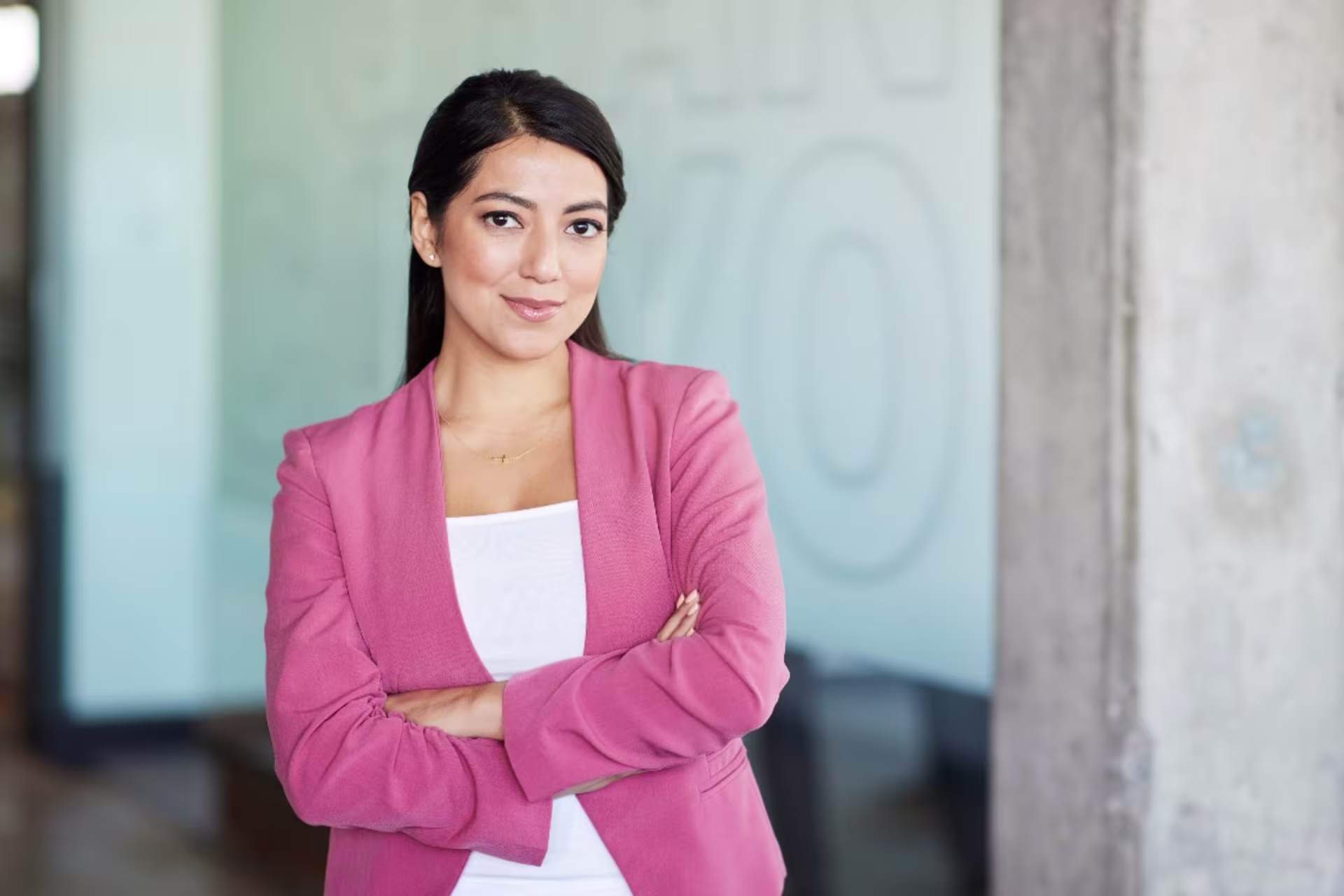 Woman finance employee in pink suit standing in office with her arms crossed 