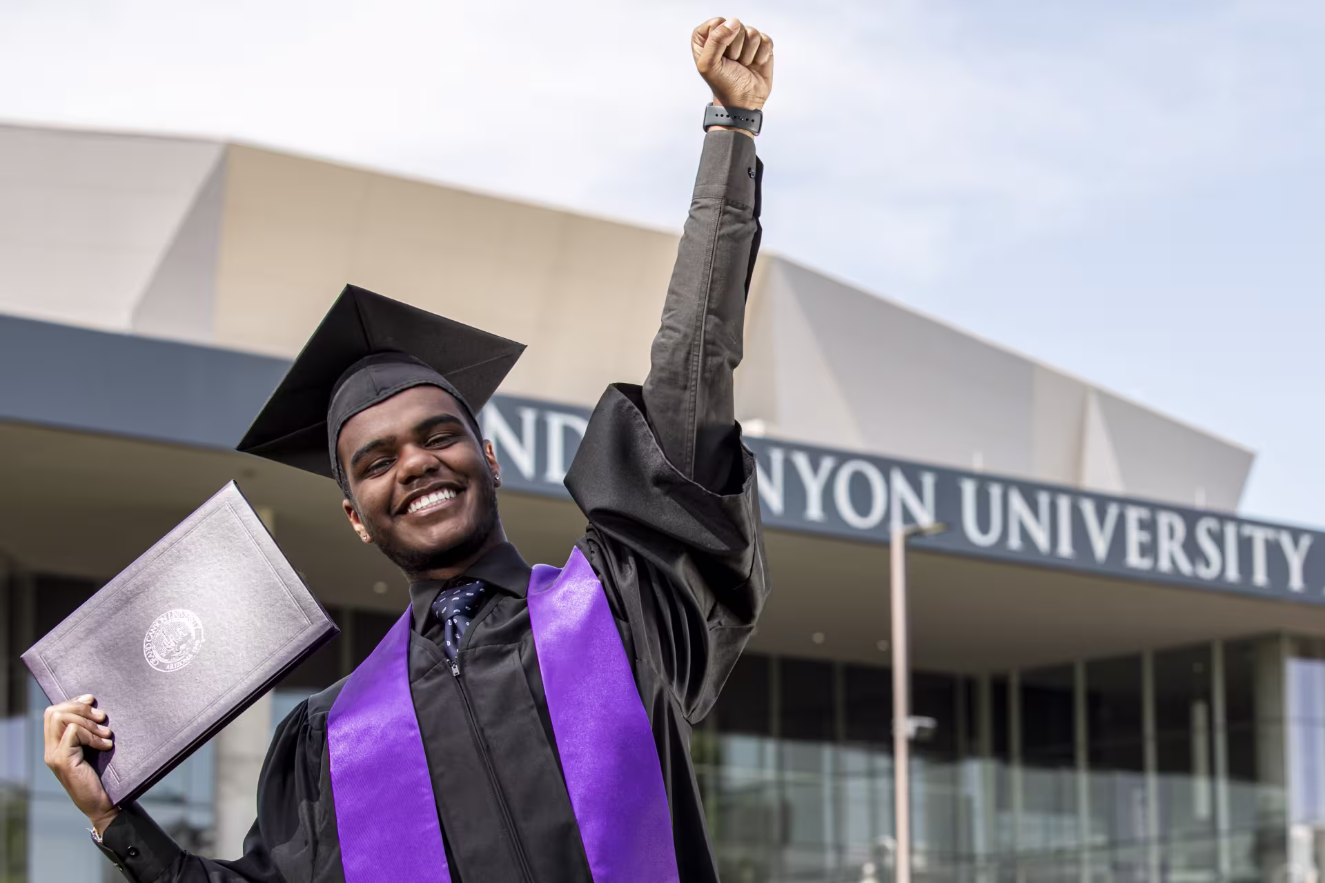 Male BS in BHS graduate smiling with arm in air at GCU commencement