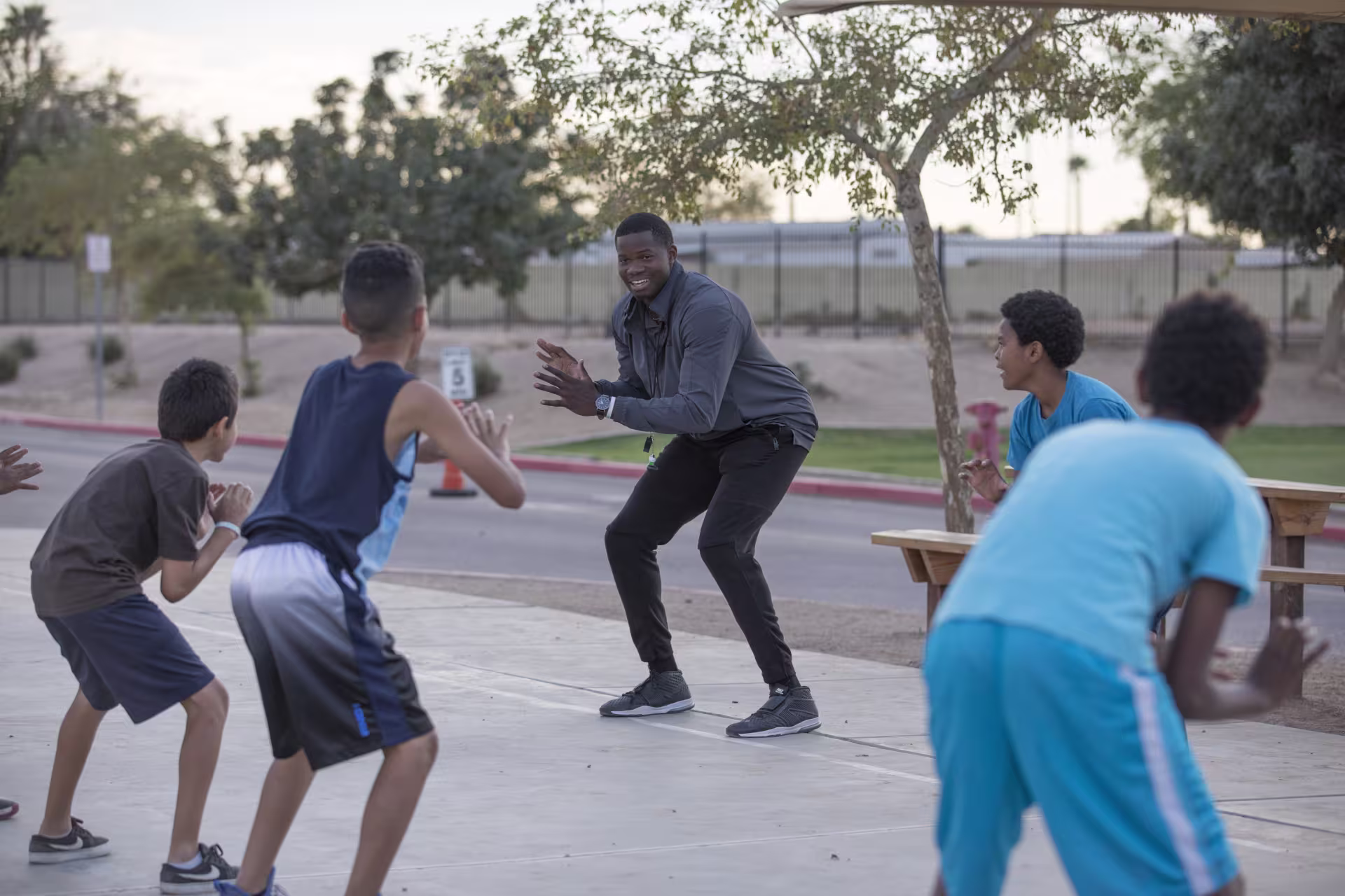 Male PE teacher coaching group of young male students on outdoor basketball court 