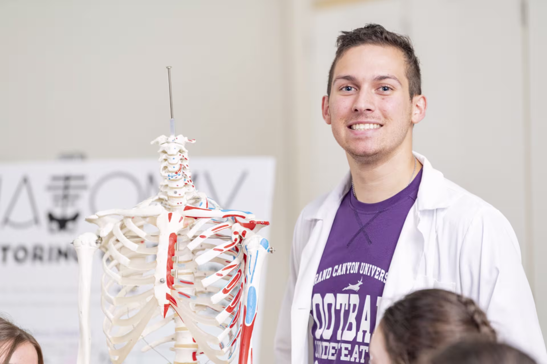 Male biology student smiling and posing beside fake skeleton