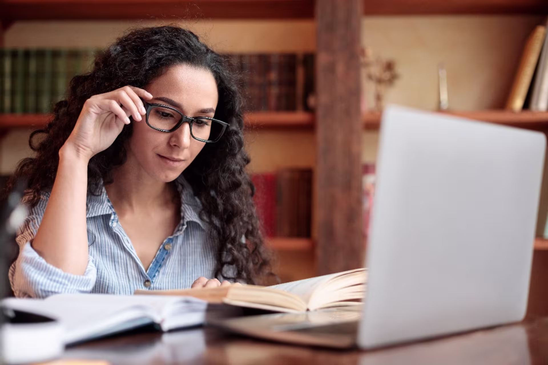 History student in glasses reading in a library with a computer