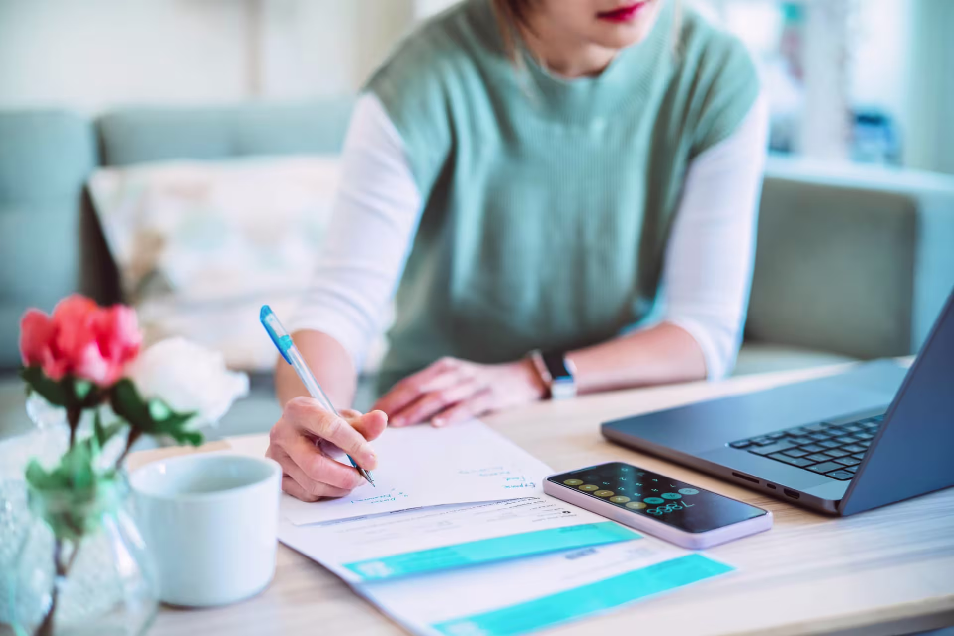A person writing on a paper while studying for an MBA in Accounting, with a laptop, phone, and coffee cup visible on the desk.