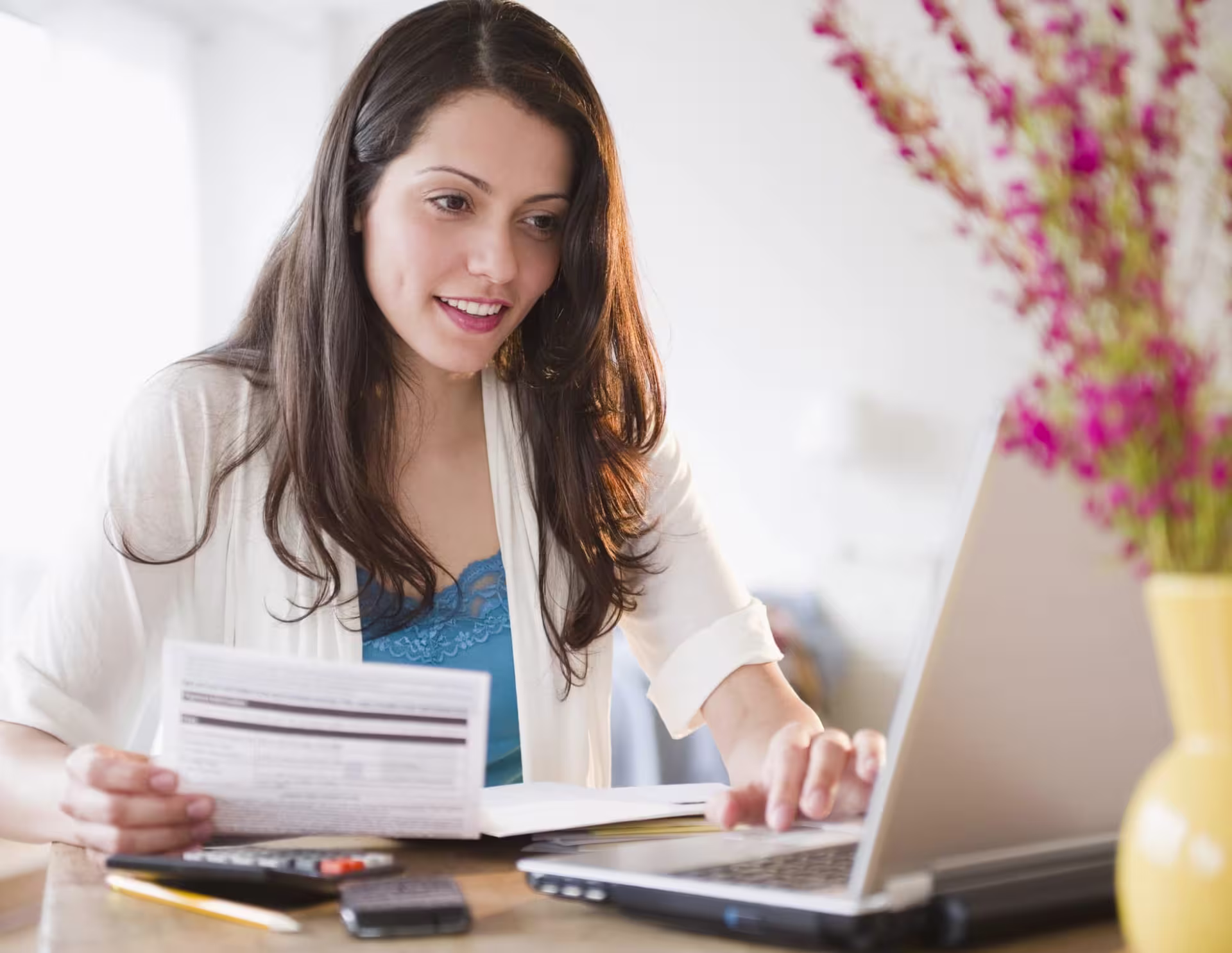 A woman reviewing financial documents while working on a laptop, representing the skills gained in an MBA in Accounting program.