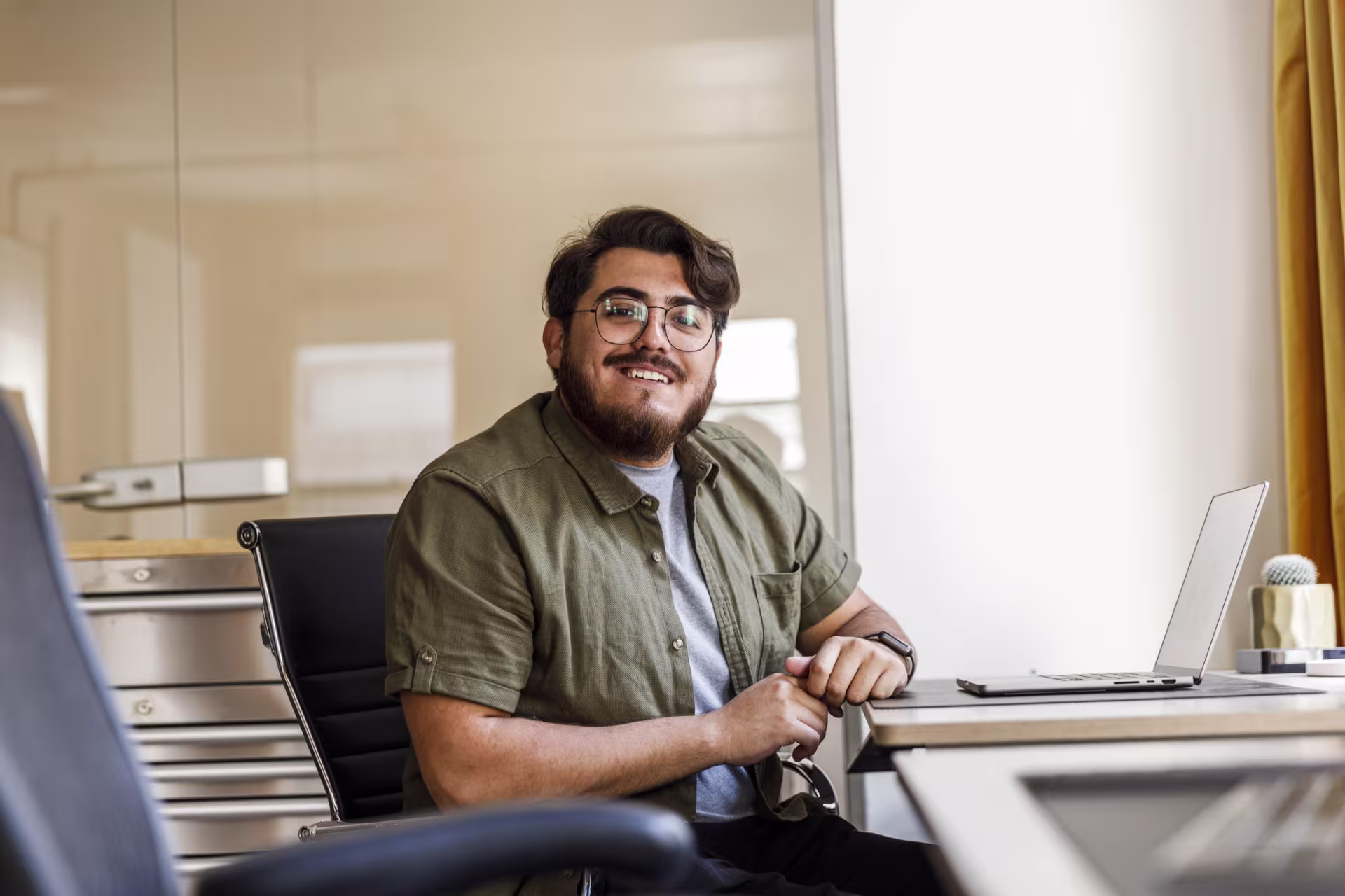 Hispanic male software development student in olive dress shirt smiles when taking a break from online programming coursework.