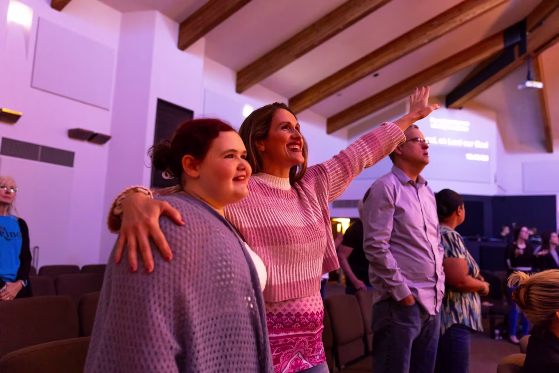 Woman with her arm around a teen as they worship in a church setting