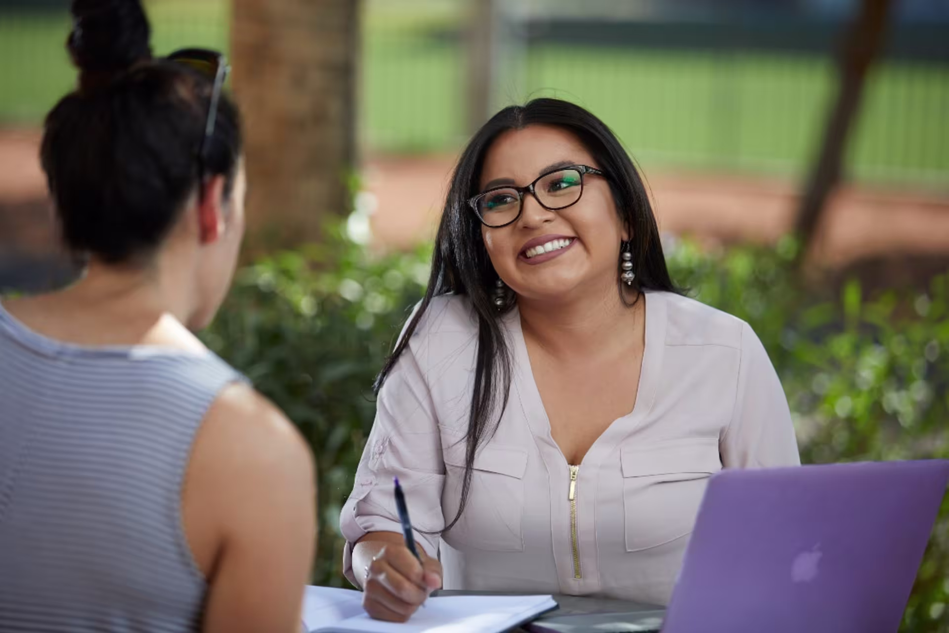 Marketing student sitting outside with laptop discussing coursework with another student