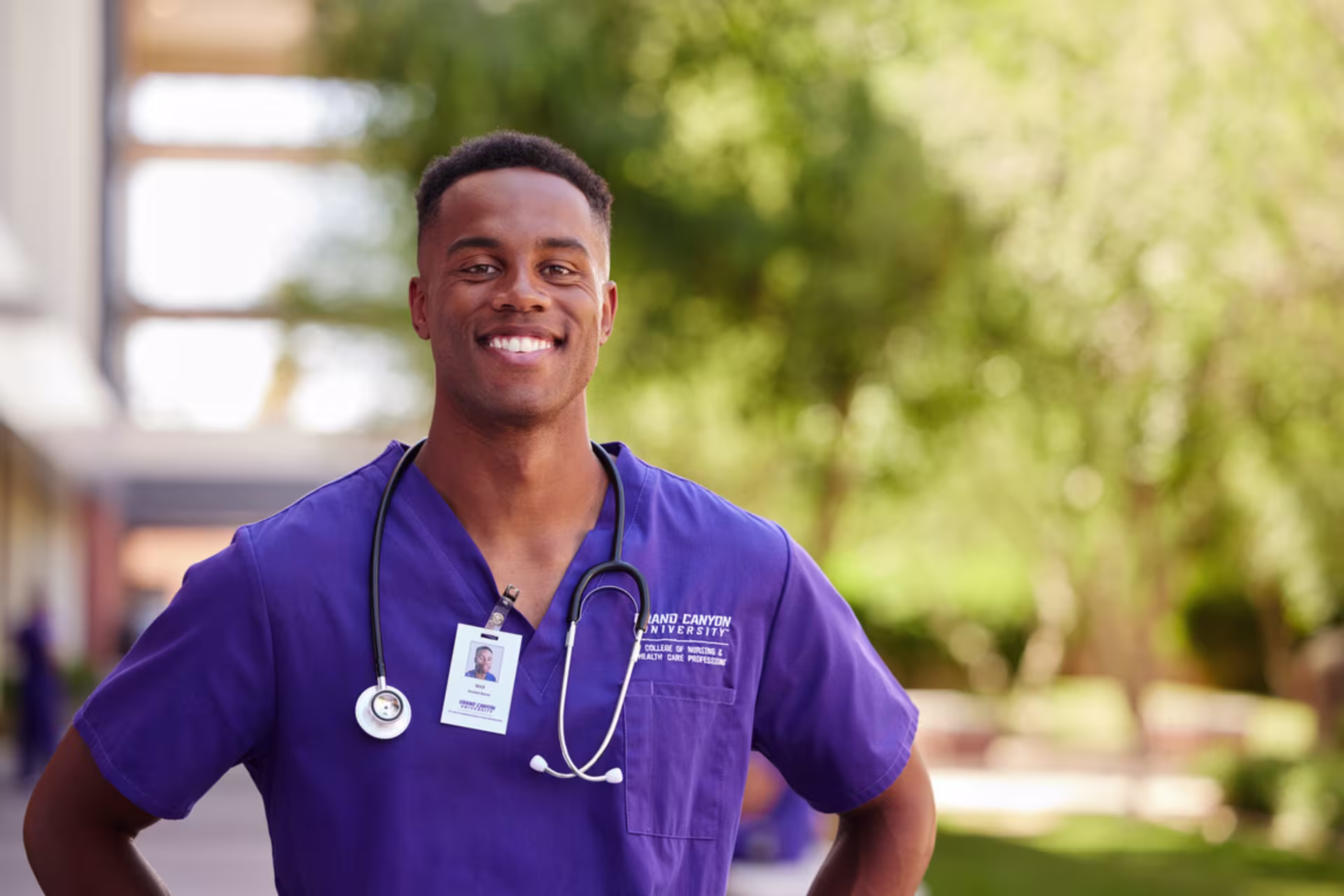 black male with hands on hips smiles in purple absn gcu student scrub