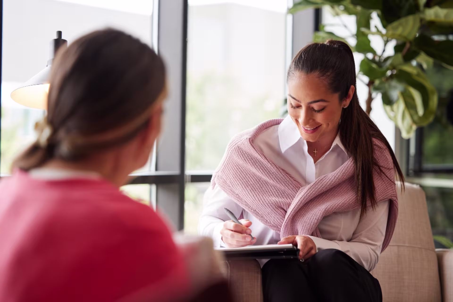 Counselor sitting in an office setting talking with a patient while taking notes