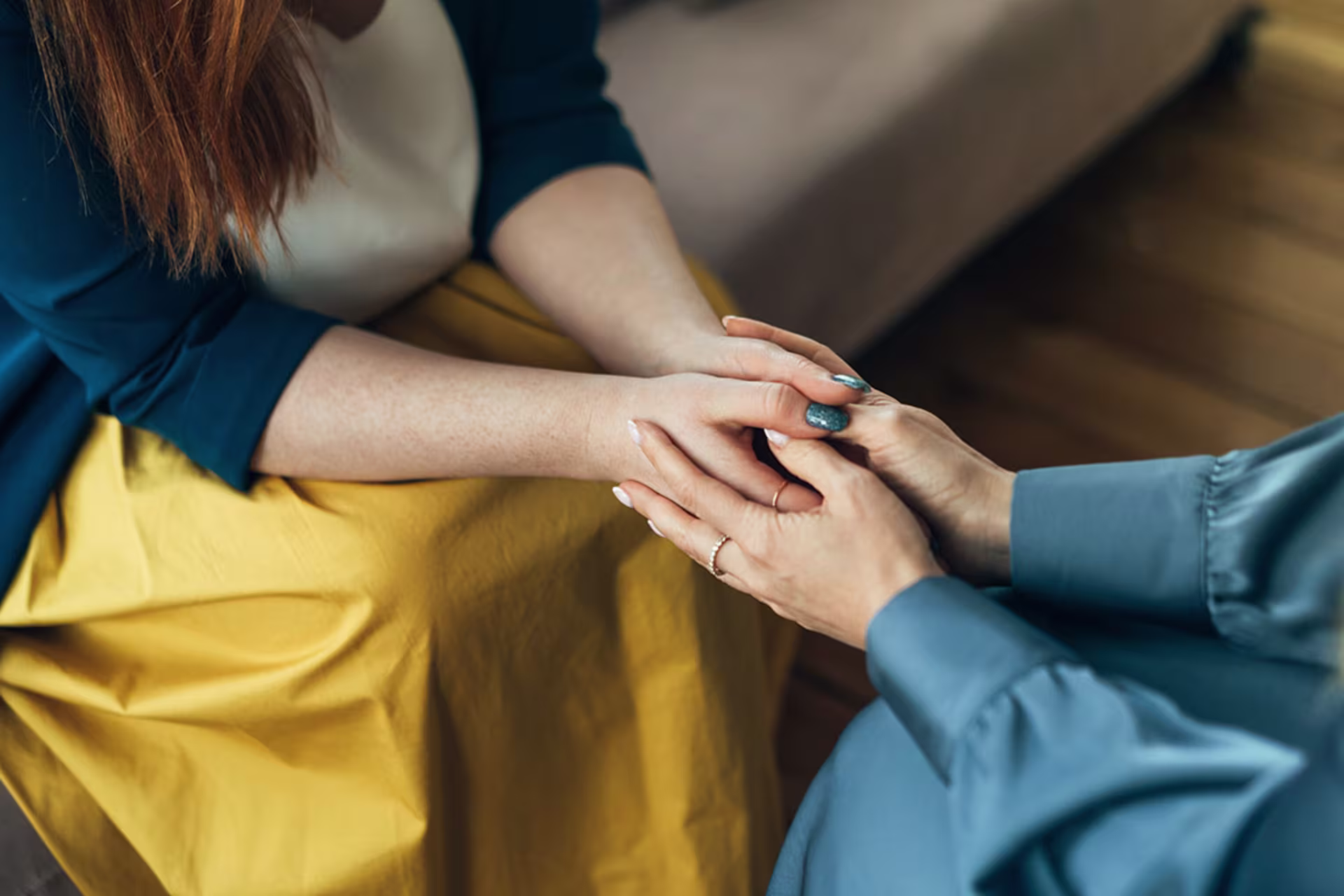 Female psychologist sitting across from female patient holding hands during therapy session